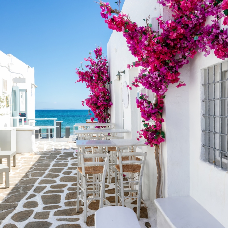White small alley and houses with red bouganvillea flowers leading to the blue sea on the cyclades in Greece, Paros island, during summer time
